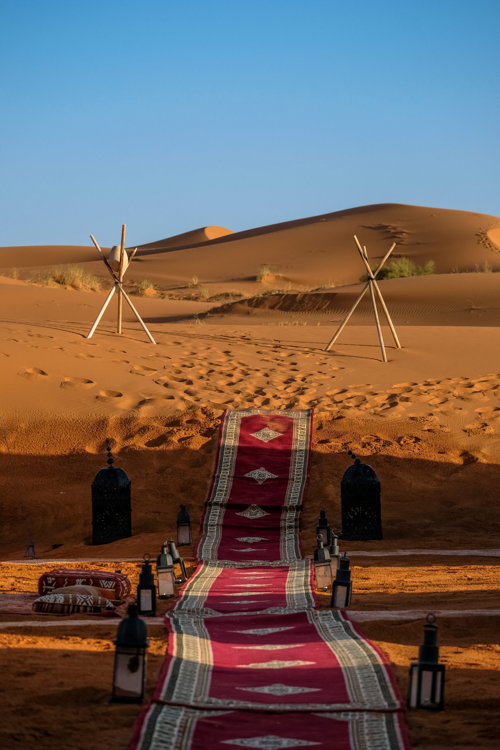 A vertical shot of a red carpet in the middle of lamps and stick tripod with a rock in the distance in the desert